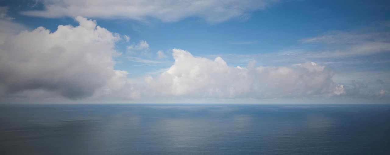 Cumulus clouds over a calm sea, the horizon low in the frame
