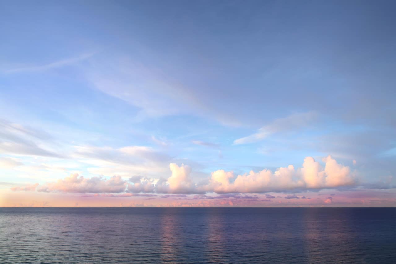 Clouds lit pink by the evening sun over a calm ocean horizon